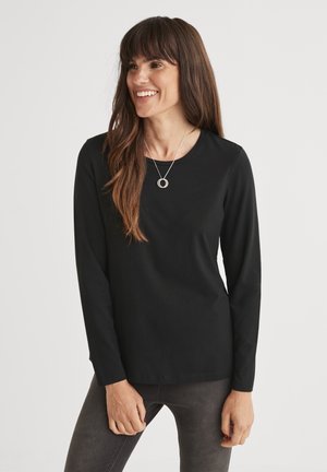 Zwarte langemouw shirt van zacht materiaal, met een ronde halslijn en een aansluitend ontwerp, gecombineerd met grijze jeans. Minimalistische look.