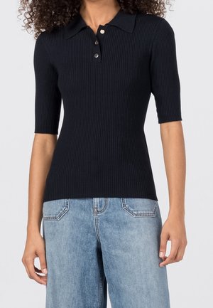 Polo shirt noir à manches courtes avec un col classique et patte de boutonnage à trois boutons, associé à un jean bleu clair avec poches arrière.