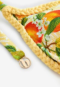 Margine împletit galben pe țesătură texturată cu model de fructe portocalii și flori albe, cu o bretea atașată prevăzută cu o încuietoare circulară aurie.