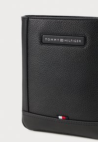 Zwart,textuurleer portfolio met een rechthoekige vorm, voorzien van een opvallend merkplaatje en een horizontale tricolore accent aan de onderkant.