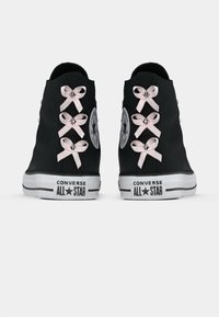 Tenisi negri din pânză cu gât înalt, cu șireturi din satin roz și ținte argintii, având un logo clasic pe latura exterioară și talpă albă.