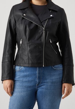 Chaqueta de cuero negra para motorista con cremallera plateada asimétrica y bolsillos laterales con cremallera, usada sobre vaqueros azules.