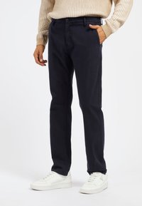 Chinos blu scuro in cotone, con taglio dritto, tasche laterali e chiusura con bottone. Abbinati a sneakers bianche.