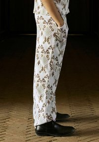 Witte met een patroon bedrukt broek met bruine en groene accenten, met een losse pasvorm en zijzakken. Gecombineerd met zwarte schoenen. De stof heeft een gestructureerd oppervlak.
