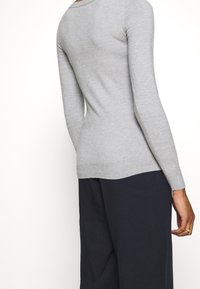 Šedý přiléhavý svetr s dlouhými rukávy, ribbenými manžetami a lemem, měkkou texturou a výstřihem do véčka, spárovaný s navy volnými kalhotami.