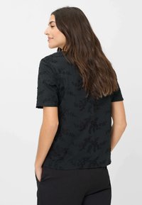 Sort kortærmet skjorte med hævet blomsterbroderi design, blød tekstur, rund halsudskæring og afslappet pasform, båret med en let drapering.