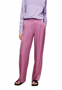 Růžové saténové kalhoty širokého střihu s předními záhyby, nošené s bledě fialovou blůzou. Mezi pozoruhodné detaily patří postranní kapsy a volný střih.