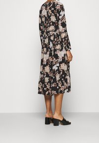 Blumendruckkleid mit langen Ärmeln, schwarzem Hintergrund, cremefarbenen und rosa Blumen, gestuftem Saum, getragen mit klobigen schwarzen Absatzmules.