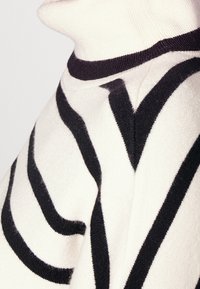Sweter w kolorze kremowym z wyraźnymi czarnymi ukośnymi paskami, z wysokim kołnierzem i prążkowanymi mankietami, wykonany z miękkiego, teksturowanego materiału.