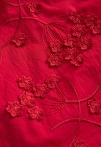 Tissu rouge présentant une broderie complexe de fleurs, avec une texture en relief et une épaisseur de fil variable, créant profondeur et détails.