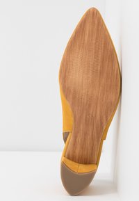 Scarpa gialla in suede con tacco alto e punta affusolata. La suola è in legno e presenta un motivo di grip testurizzato.