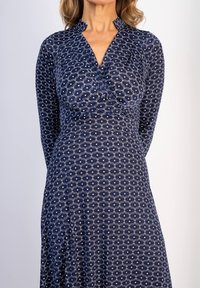 Merimiespuku, jossa on valkoinen aaltoileva kuvio, kaulus, tiukka vartalo-osa ja löysä helma. Valmistettu pehmeästä kankaasta, jossa on hieno kiilto.