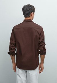 Brun langærmet skjorte med en afslappet pasform, rund kant og opkrøllede ærmer, lavet af glat stof. Bagfra, ensfarvet design, ingen mønstre.