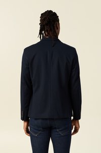 Marinblå blazer med en skuren passform, traditionella revers, ryggslits och knäppta manschetter, tillverkad av textil med struktur, i kombination med mörka jeans.