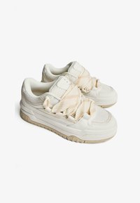 Witte sneakers met een gestructureerde mesh bovenkant en zachte leren accenten. Voorzien van een kruislings strapdesign en een lichtbruine rubberen zool.