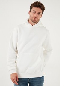 Hvid hættetrøje lavet af blødt stof med kængurulomme og snøre i hætten. Pasformen er løs med ribstrikkede manchetter og kant.