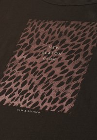 T-shirt with brown animal print rectangle and white text reading "New Season Club" and "Raw & Refined" on dark fabric.