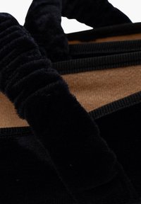 Bolsa de terciopelo negro con una superficie suave y texturada. Presenta asas negras fruncidas y un interior en tono marrón claro. Costuras duraderas a lo largo de los bordes.