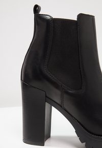 Bottine noire en cuir avec talon haut épais, panneau latéral élastique et languette à l'arrière.