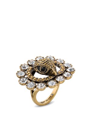 Anello in tonalità oro con motivo a occhio, circondato da pietre chiare di forma circolare. La base presenta una finitura testurizzata con dettagli intricati.