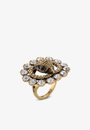 Anello in tonalità oro con motivo a occhio, circondato da pietre chiare di forma circolare. La base presenta una finitura testurizzata con dettagli intricati.