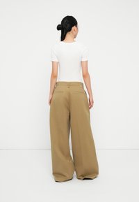 Pantaloni khaki a gamba ampia con vita alta, tessuto piegato e tasche frontali, abbinati a una maglietta bianca aderente.
