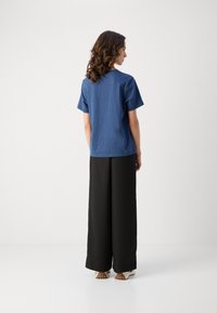Blue short-sleeve top with a textured finish, paired with high-waisted black wide-leg trousers and light-colored footwear.