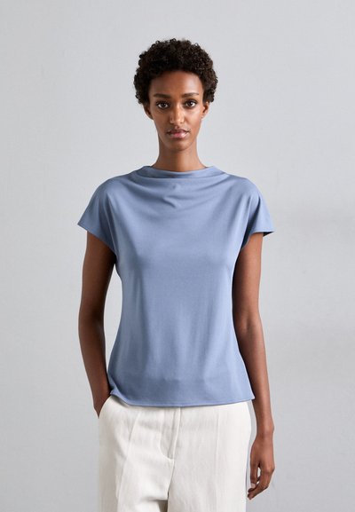 Haut à manches courtes bleu clair en tissu lisse, avec un col rond et une coupe décontractée, associé à un pantalon de couleur claire.