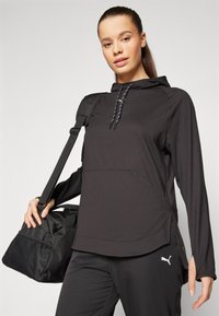 Svart huvtröja med långa ärmar, utrustad med en känguruficka och sidslitningar. Inkluderar en reflekterande dragsko och Puma-logotyp.