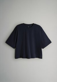 Marineblaues, kurz geschnittenes T-Shirt aus weicher Baumwolle mit rundem Ausschnitt und kurzen Ärmeln in lockerer Passform. Minimalistisches Design, ohne Muster.