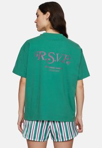 Grøn oversized T-shirt i bomuld med "R.S.V.P." i pink på ryggen, parret med multikolorede stribede shorts.