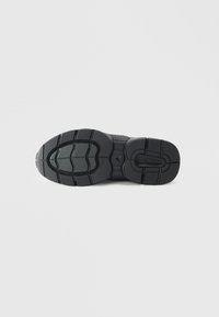 Talpa de sneaker neagră cu cauciuc texturat, featuring caneluri pentru tracțiune, modele circulare și detalii contrastante cu logo-ul. Design simplu și robust.