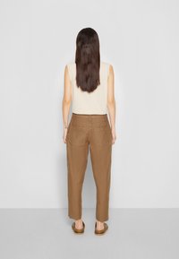 Beige mouwloze top gecombineerd met bruin, semi-getailleerde cargobroeken met twee achterzakken. Het model is van achteren te zien.