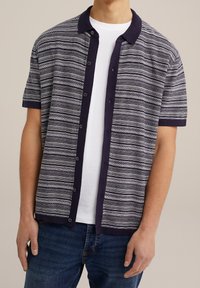 Chemise à manches courtes à boutons en bleu marine avec un motif rayé blanc et gris, présentant un col contrastant et un tissu texturé.