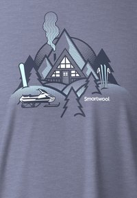 Camiseta gráfica gris con diseño de una cabaña, montañas y una moto de nieve. Los diseños incluyen formas geométricas, líneas y árboles, con el logo de "Smartwool".