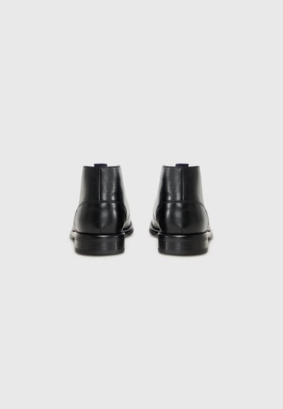 Bottines en cuir noir avec une finition lisse, bout arrondi et un petit talon empilé. Présente une couture minimale et une languette à l'arrière.