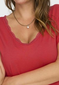 Červený top s krátkým rukávem a výstřihem do V lemovaným krajkou, doplněný řetízkem s přívěskem ve tvaru kapky z perly. Hladká textilie.