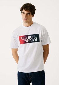 Balta kokvilnas t-kreklā ir krāsains "RED BULL RACING" grafiskais attēls sarkanā un zilā krāsā. Īsas piedurknes un apaļais kakla izgriezums.