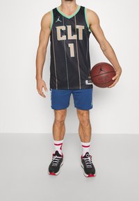 Maillot de basket-ball noir avec des accents turquoise, "CLT" et "1" sur le devant. Porté avec un short bleu, des chaussettes blanches à rayures rouges et des baskets noires.