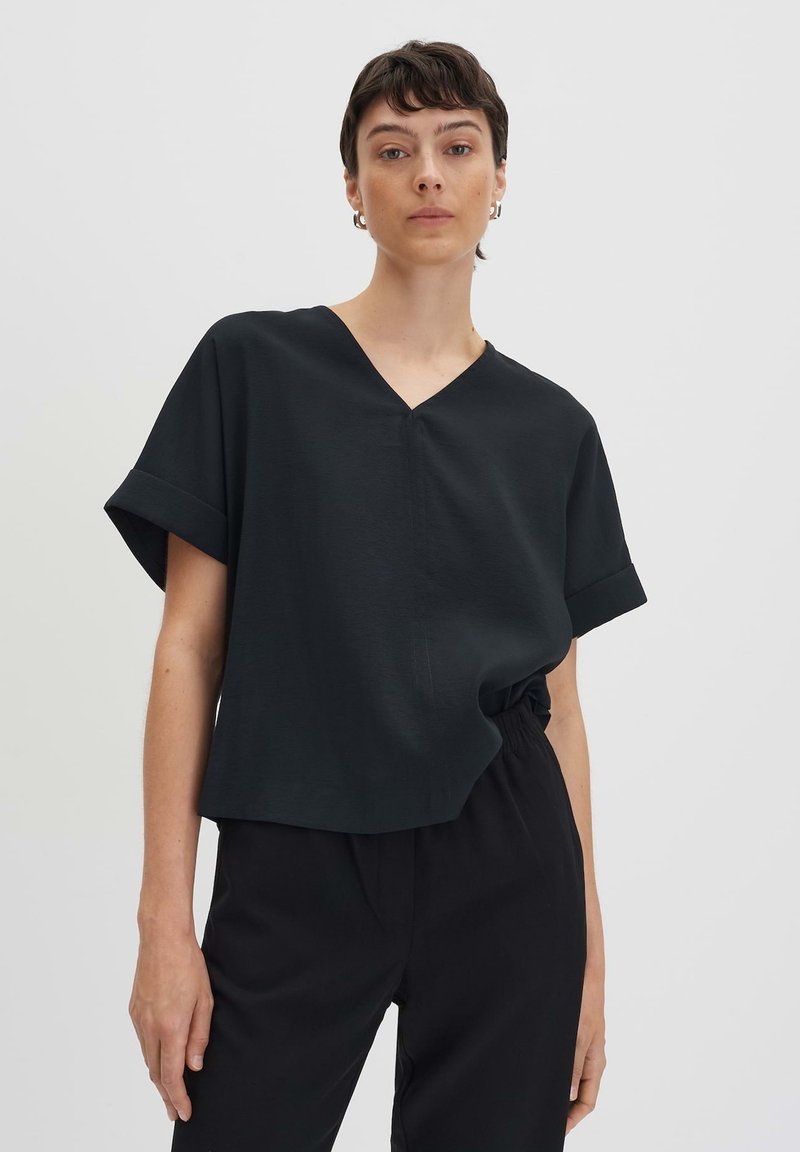 Top nero a maniche corte con scollo a Vrealizzato in tessuto morbido, caratterizzato da una vestibilità comoda e un sottile dettaglio di cucitura anteriore, abbinato a pantaloni neri.