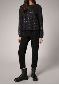 Suéter negro con lentejuelas y cuello redondo, combinado con pantalones negros ajustados y botas de combate negras con cordones. Textura lisa, ajuste casual.