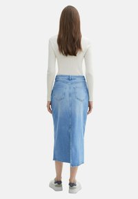 Light blue denim skirt with a straight cut, back pockets, and a mid-calf length. Paired with white ribbed long-sleeve top and sneakers.
