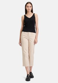 Débardeur noir à côtes avec un col en V et des accents scintillants subtils, associé à un pantalon beige à taille haute et jambes larges, et des chaussures noires chunky.