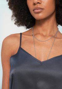 Σκούρο γκρι σατέν καμιζόλ με λεπτές τιράντες και σχέδιο λαιμόκοψης σε σχήμα V, με λεία υφή και πολύστρωτο ασημένιο κολιέ με αλυσίδες.