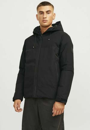 Chaqueta con capucha negra hecha de tejido texturizado, que cuenta con cierre de cremallera, bolsillos con cremallera y puños elásticos. Diseño simple y funcional.