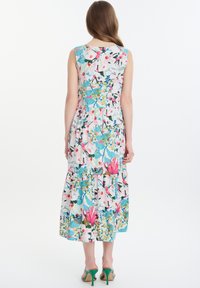 Blumenkleid ohne Ärmel mit gestuftem Saum; zeigt blaue, pinke und grüne Muster auf einem hellen Hintergrund; ergänzt durch grüne Absätze.