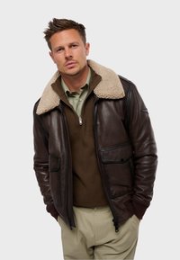 Chaqueta bomber de cuero marrón con cuello de borreguito crema, cierre de cremallera, dos bolsillos frontales y puños y dobladillo acanalados.