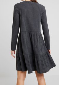 Mörkgrå långärmad klänning med ribbat mönster, lager-på-lager utsvängd kjol, rund halsringning och subtila horisontella ränder.