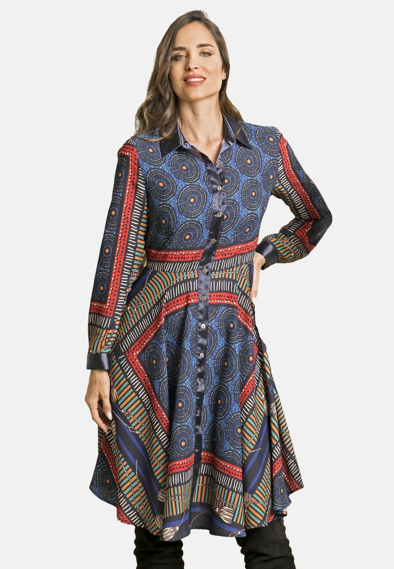 Vestido de camisa multicolorido con patrones circulares y geométricos en azul, rojo y verde. Mangas largas y botones frontales, ajustado en la cintura.