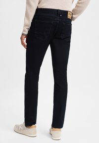 Jeans en denim noir ajustés avec une texture lisse, dotés de deux poches arrière et d'une étiquette en cuir de marque à la taille.
